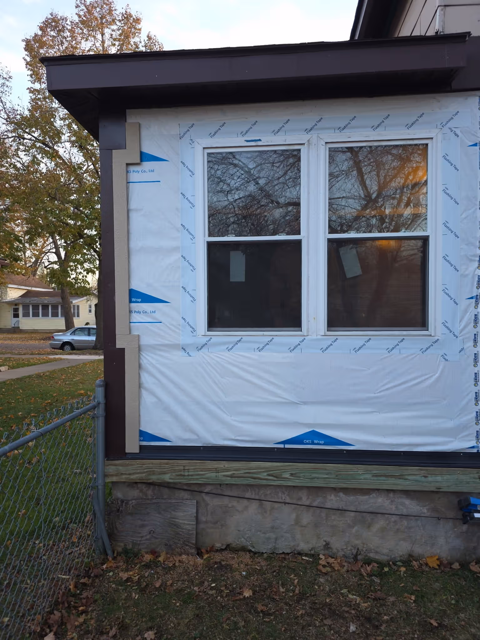Window with white frame on a house wall covered in white construction wrap with flashing tape.