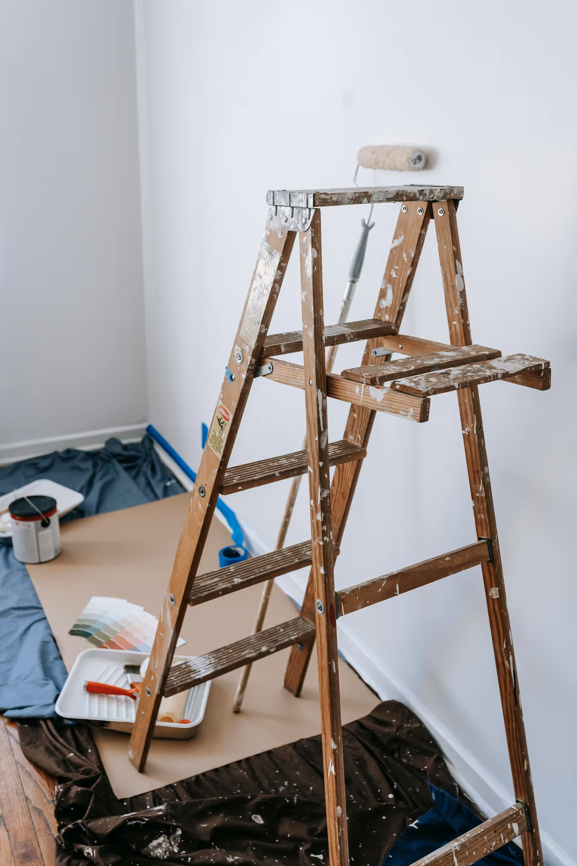 Wooden step ladder with paint splatters amidst painting supplies and color swatches in a room.