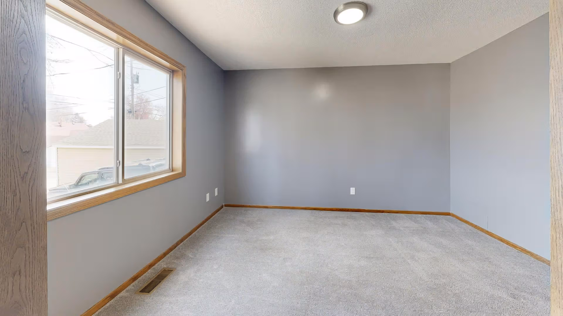 Empty room with gray carpet, gray walls, wooden trim, large window, and ceiling light.
